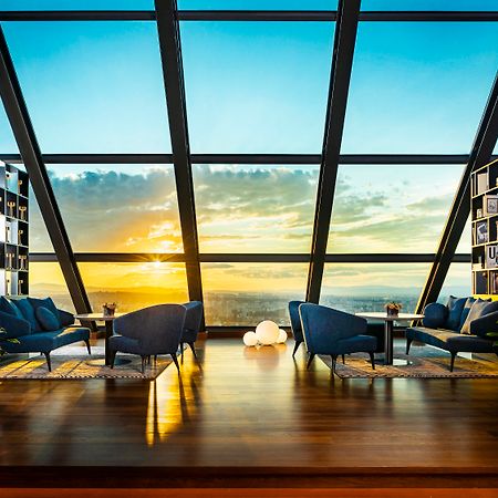 Grand Hotel Millennium 索菲亞 外观 照片 The photo depicts a modern, stylish interior of a high-rise space with a panoramic view through large glass windows. The scene features a cozy seating area with several blue armchairs arranged around a low table, creating a comfortable atmosphere. Th