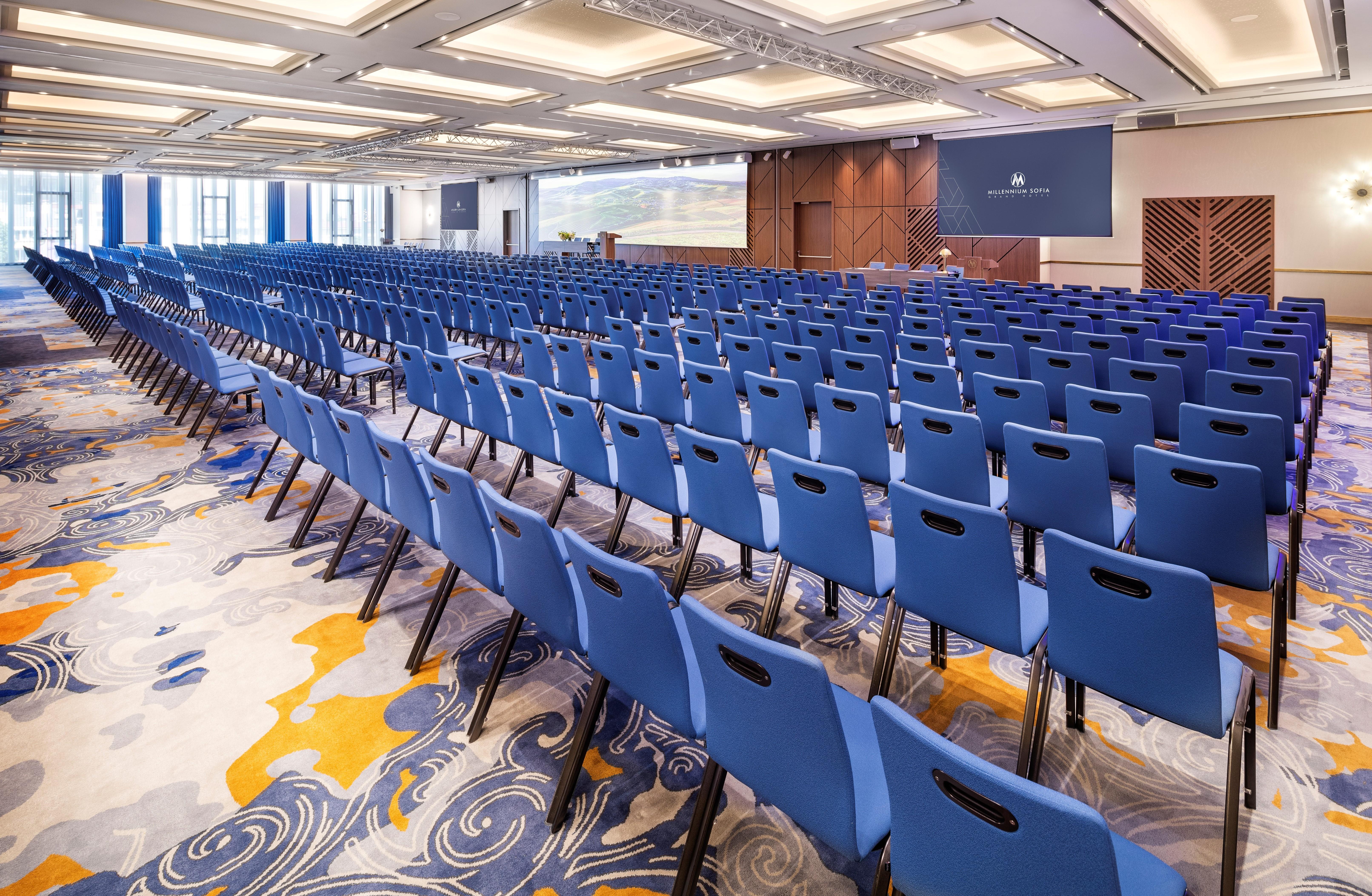 Grand Hotel Millennium 索菲亞 外观 照片 The photo shows a large conference or meeting room set up for an event. There are numerous blue chairs arranged in rows, creating a seating area for attendees. The floor features a decorative pattern, and the room has a modern design with ample light