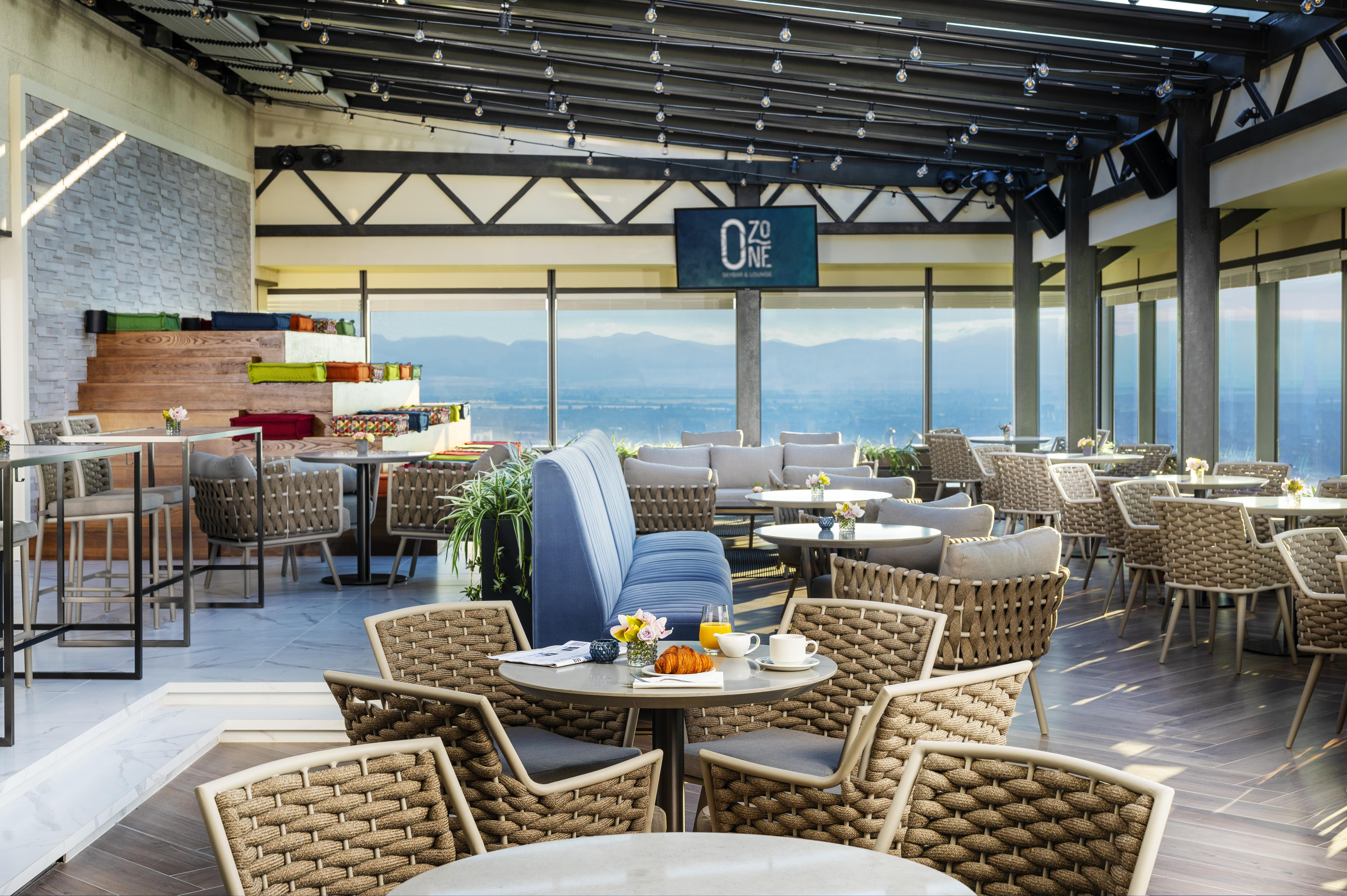 Grand Hotel Millennium 索菲亞 外观 照片 The photo shows a modern restaurant or café with a spacious interior. It features a variety of seating arrangements, including round tables surrounded by wicker chairs and lounges. Large windows allow for a panoramic view, which likely includes sceni